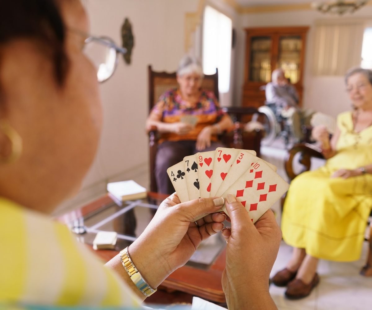 Old people in geriatric hospice: group of senior women playing cards and having fun together. The aged ladies sit on the sofa of the hospital and start a new match